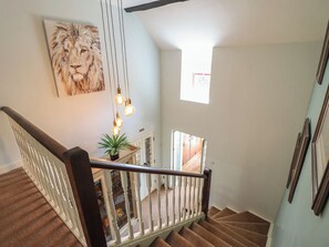 A staircase with a wooden handrail, a potted plant, and a painting of a lion's face on the wall. - Bryn Y Garreg Cottage - The Wireless Free Farm (Welshpool)
