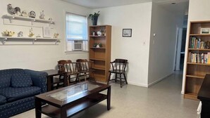 A living room with a dark wooden coffee table, a blue sofa, two wooden chairs, a bookshelf, and a window with blinds. - “The Retreat” with two balconies free parking (Atlantic City)