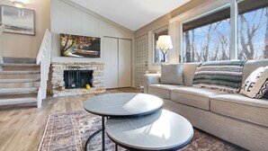 A living room with a fireplace, a sofa, a coffee table, and a staircase. - Escape to Abbey Springs! 2 bedroom, 1 Bath Condo in Private Gated Community (Fontana-on-Geneva Lake)