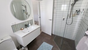 A bathroom with a white sink, mirror, and shower. - Absolute beach front comfort and luxury. (Waihi Beach)