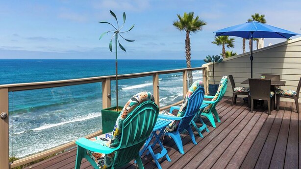 Une terrasse avec des chaises turquoise et une table, d’où l’on a une vue sur l’océan.