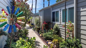 Un jardin résidentiel agrémenté d’un moulin à vent aux couleurs vives, de différentes plantes et d’un sentier menant à une maison dotée de fenêtres et d’une porte.
