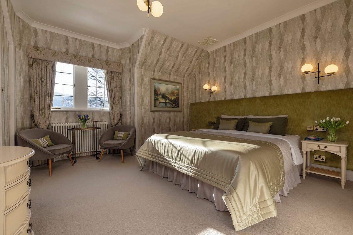 A bedroom with a large bed, two chairs, a dresser, a radiator, and a window.