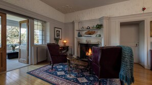 A room with a fireplace, two chairs, a table, and a patterned rug.