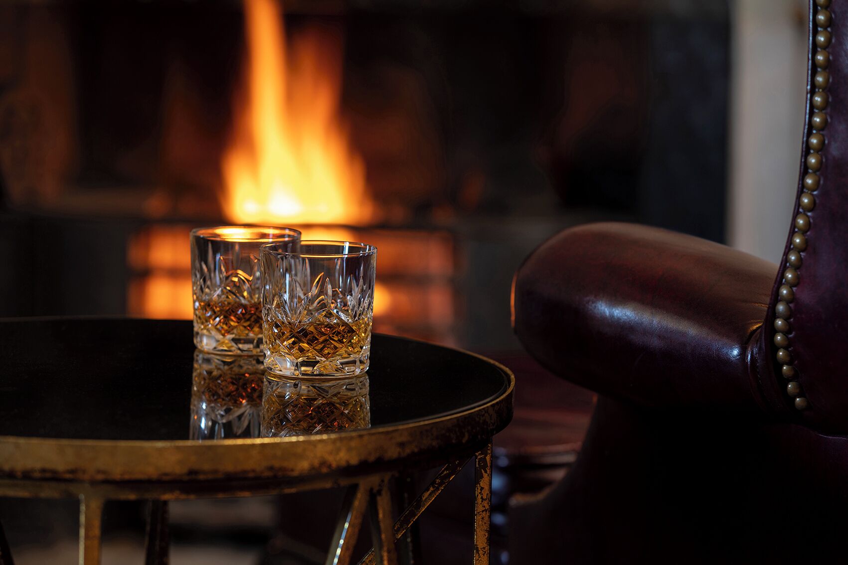 Ein Tisch mit zwei Whiskeygläsern, ein Ledersessel und im Hintergrund ein Kamin.