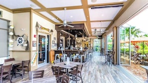 Ein großzügiger Innenbereich mit Holzböden, mehreren Tischen und Stühlen, einer Bar und großen Fenstern mit Blick ins Freie.