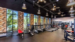 Ein Fitnessraum mit Trainingsgeräten, großen Fenstern und einer Ziegelwand.