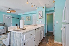 Une cuisine dotée d’un îlot central, de meubles blancs, d’un évier et d’un ventilateur de plafond.