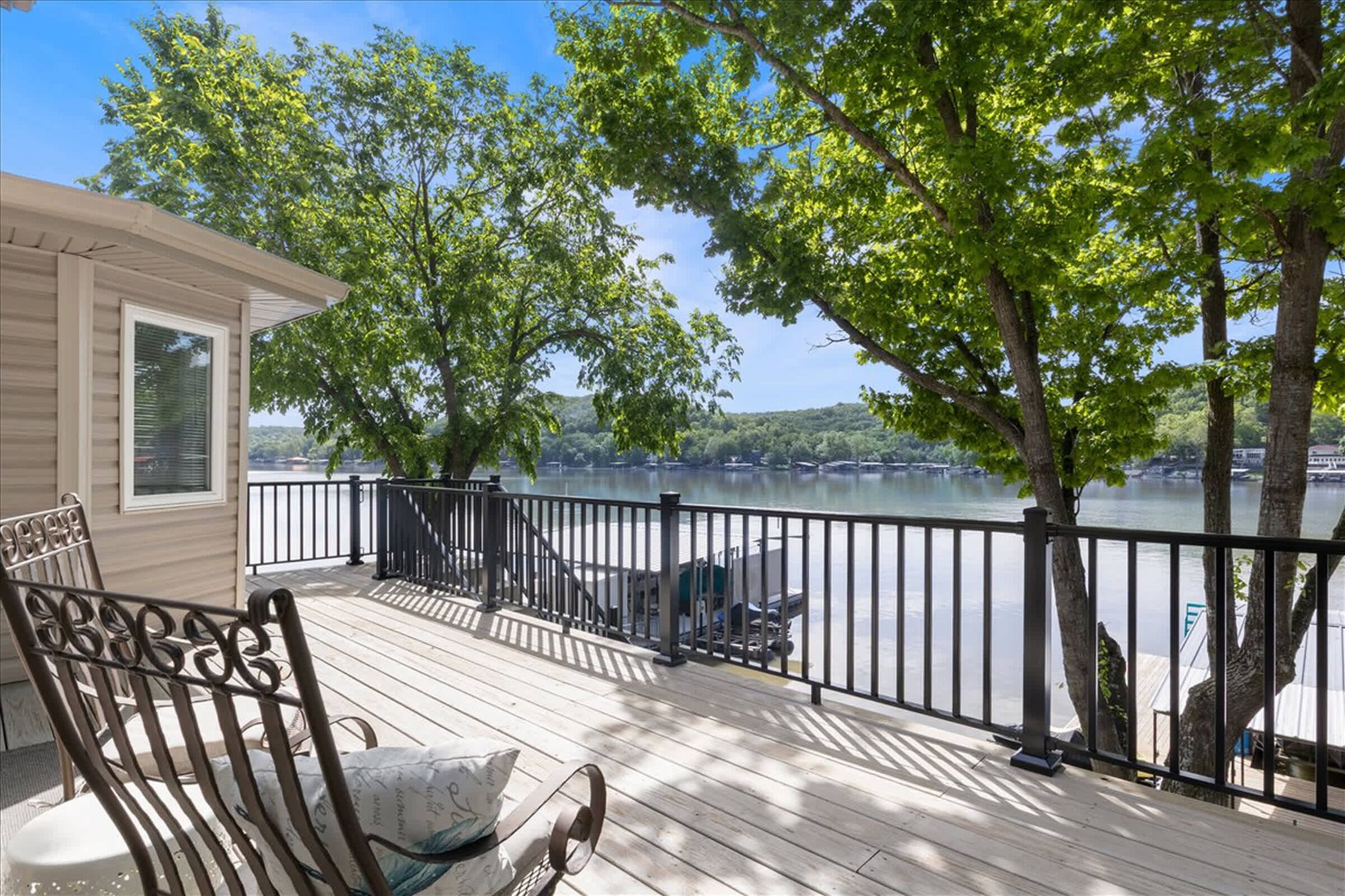 A wooden deck with a metal railing, overlooking a calm lake with boats and trees.