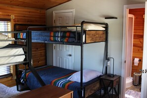 A bunk bed room with a wooden door, a small table, and a lamp.