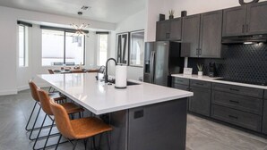 A modern kitchen with a large island, dark cabinetry, and a black backsplash. - Havasu Hideaway: Modern Lux, Pool+Spa, Near Marina (Lake Havasu City)