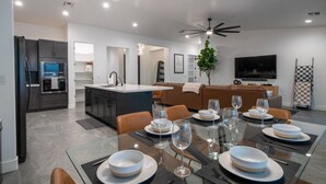 A modern kitchen with a built-in oven and microwave, a dining area with a glass table set for six, and a living area with a sofa and TV. - Havasu Hideaway: Modern Lux, Pool+Spa, Near Marina (Lake Havasu City)