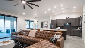 A modern living room with a brown leather sectional sofa, a round coffee table, and a dining area with a white table and chairs. - Havasu Hideaway: Modern Lux, Pool+Spa, Near Marina (Lake Havasu City)