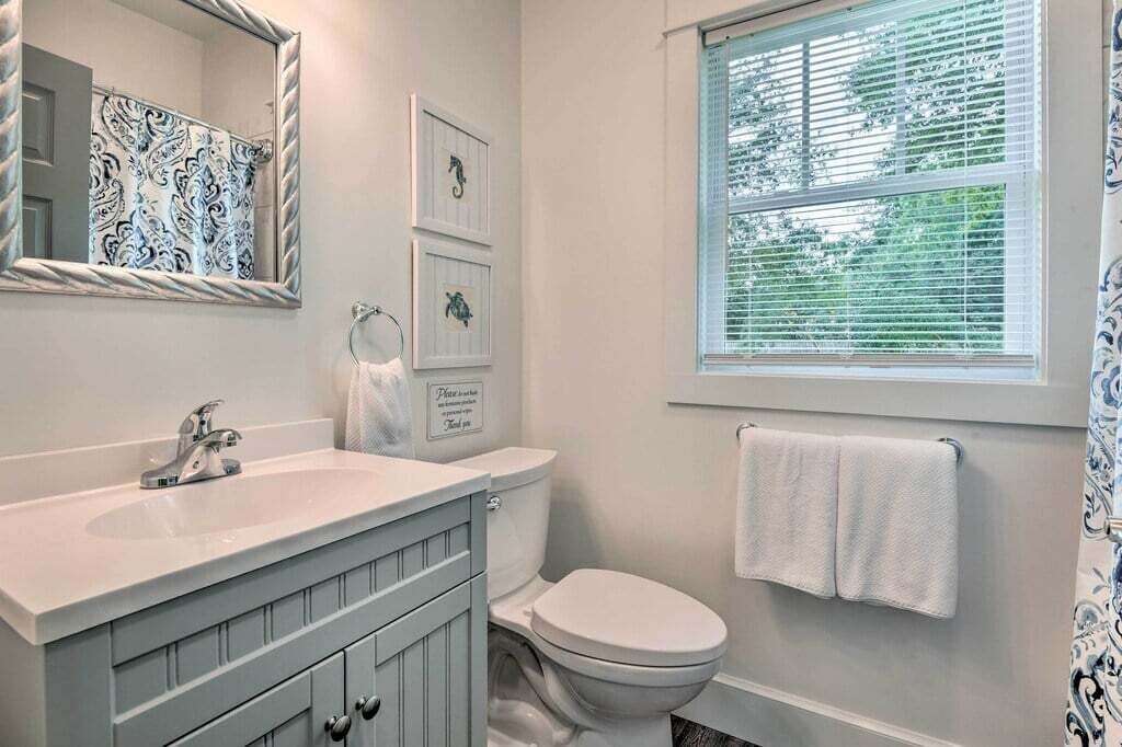 A bathroom with a white sink, a toilet, a mirror, and a window with blinds.