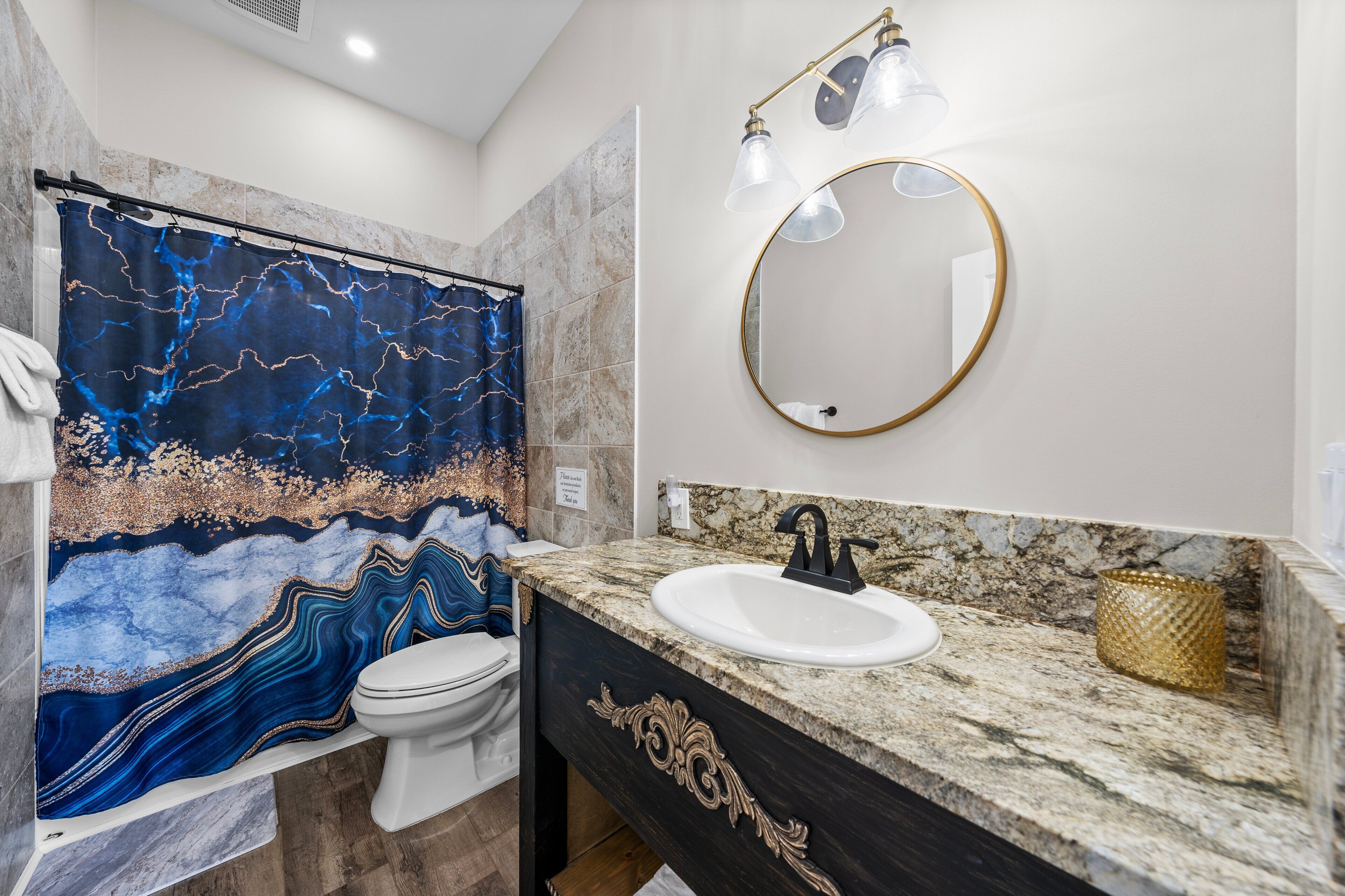 Een badkamer met een marmeren wastafel, een spiegel met gouden lijst en een douchegordijn met een abstract ontwerp in blauw en goud.