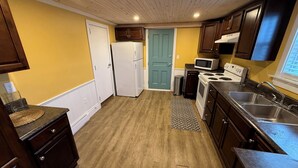 A compact kitchen with wooden cabinets, a refrigerator, microwave, stove, and a sink. - The Historical William Ellis Saint House (Bonavista)