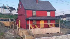 A two-story red house with a front porch and a small staircase leading to the entrance. - The Historical William Ellis Saint House (Bonavista)