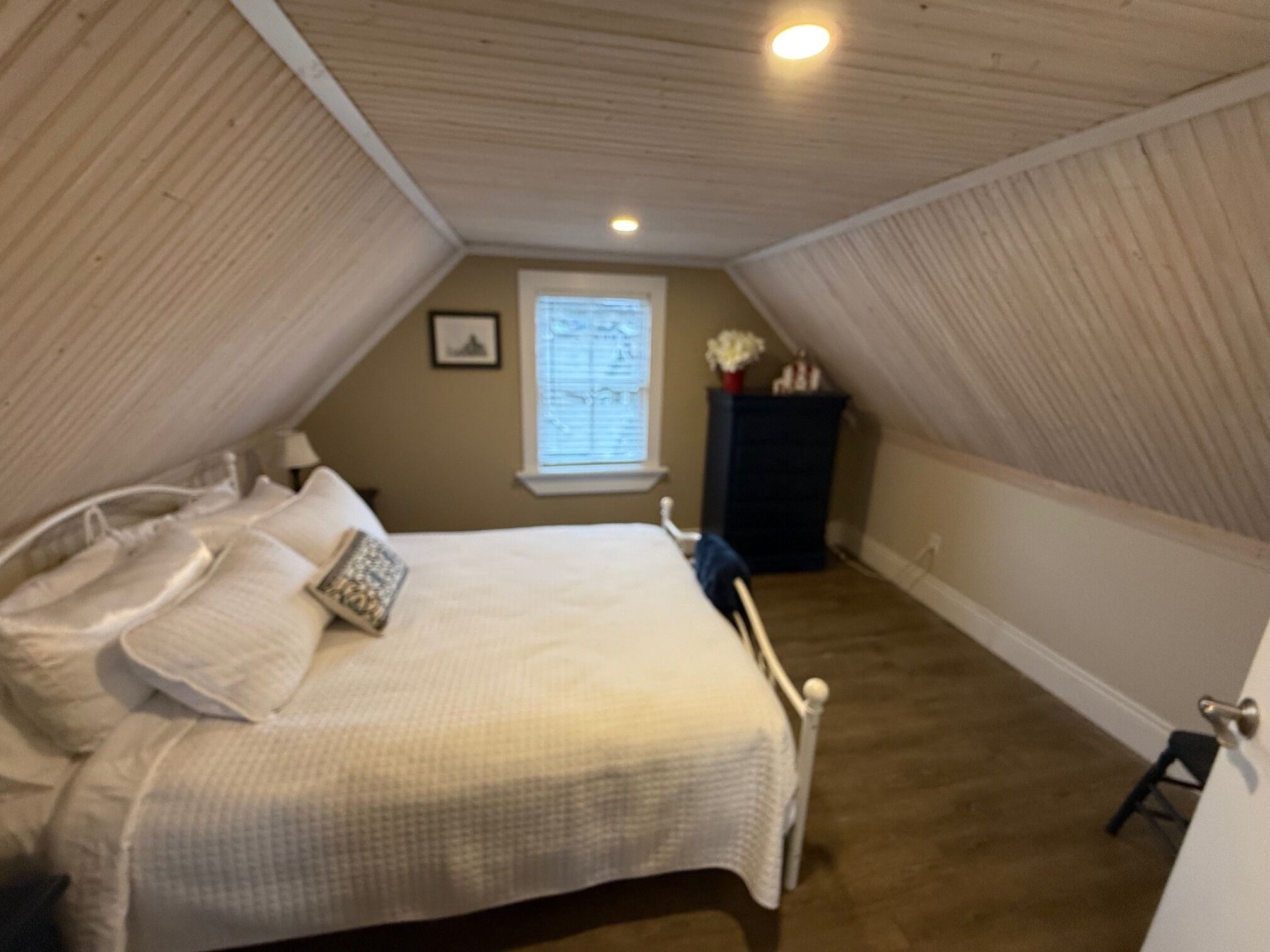 A bedroom with a bed, pillows, a nightstand, a window, and a dark cabinet.