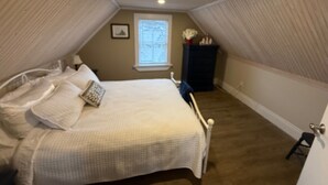 A bedroom with a bed, pillows, a nightstand, a window, and a dark cabinet. - The Historical William Ellis Saint House (Bonavista)