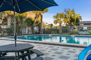 A swimming pool with a tiled deck, surrounded by palm trees and a fence. - Batiki West: Steps to Beach, Gulf Views + Pool! (Fort Myers Beach)
