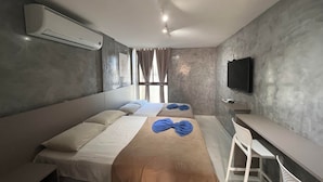 Hotelkamer met een bed, bureau, stoel, airconditioning, televisie en een raam met gordijnen.
