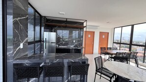 A modern kitchen with a large island, black marble countertops, and a stainless steel refrigerator. There is a dining area with a round table and black chairs. - Flat Comfort La Belle Formosa - Cabedelo (Cabedelo)