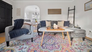 A living room with a gray sofa, a blue armchair, a coffee table, and a colorful rug. - Appealing 2br Cape Cod w/ bonus rm & fiber Wi-Fi! (Toledo)