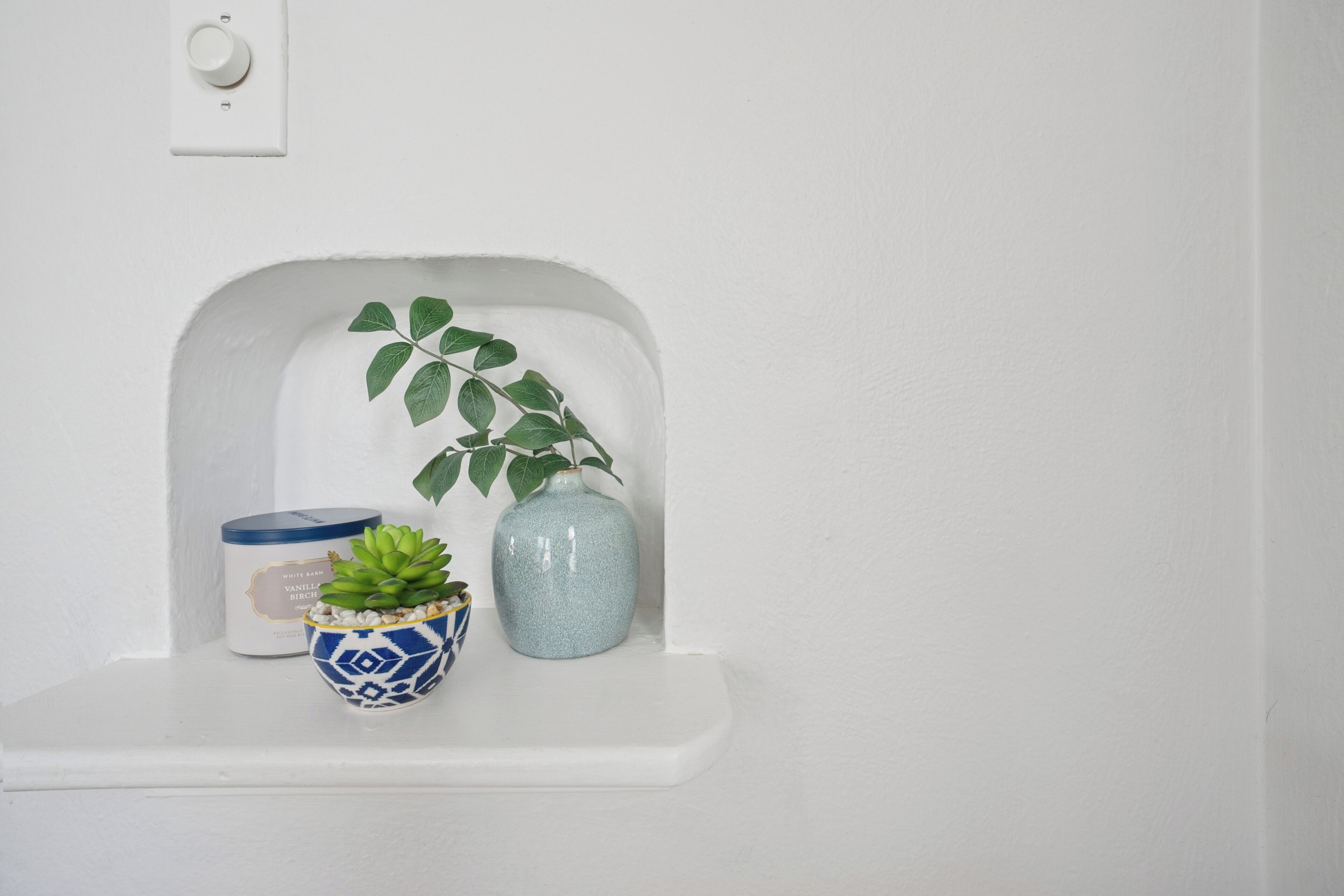Een wit plankje met een kleine plant in pot en een decoratieve vaas.