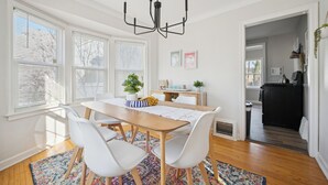 A dining area with a wooden table, white chairs, a colorful rug, and a black chandelier. - Appealing 2br Cape Cod w/ bonus rm & fiber Wi-Fi! (Toledo)