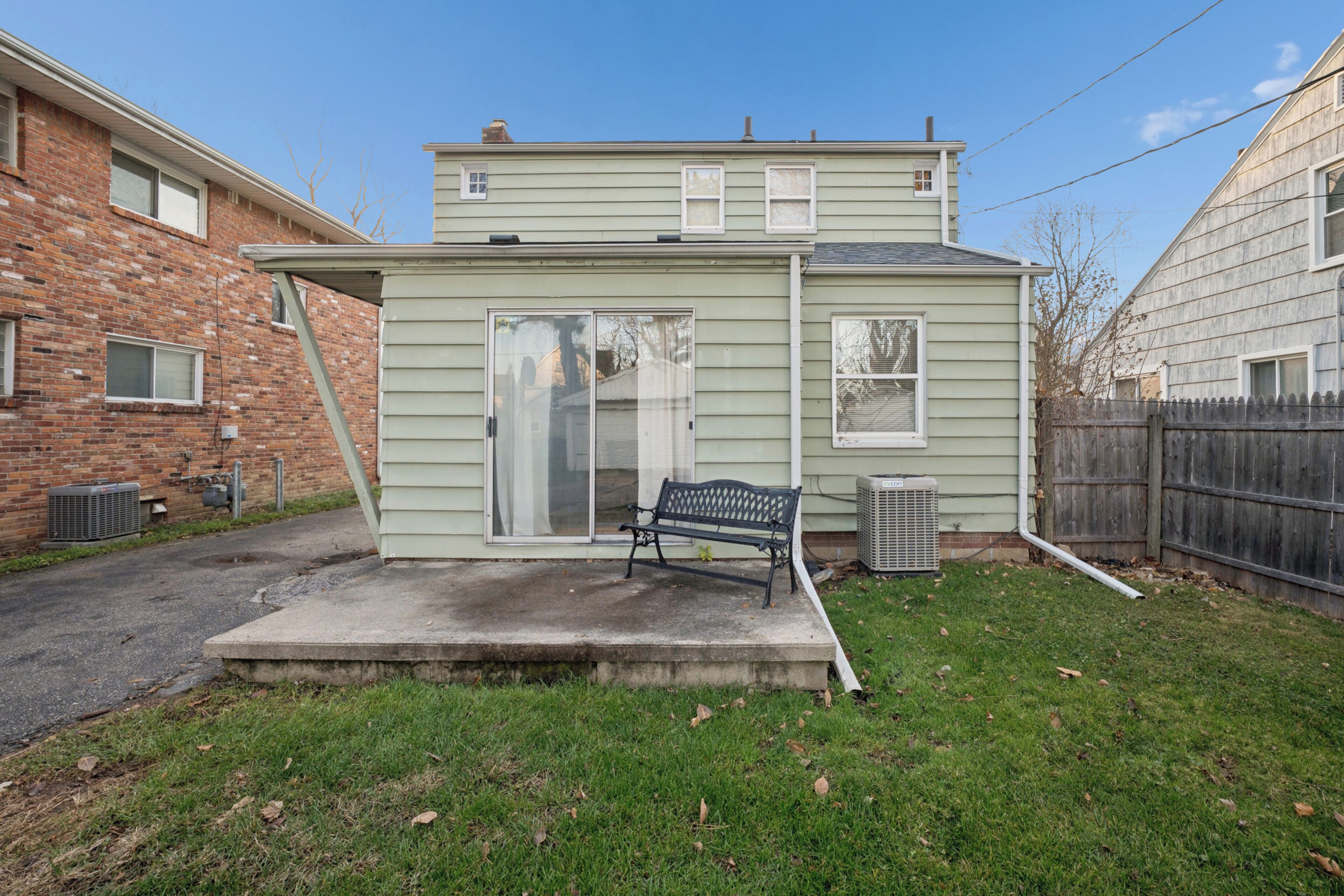 A small, single-story house with a front porch, a bench, and a sliding glass door.