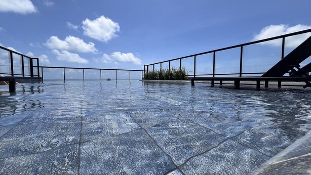 An infinity pool with a clear view of the ocean, surrounded by a metal railing and a small garden area. - Flat Premium Legacy Suites - Cabo Branco (João Pessoa)