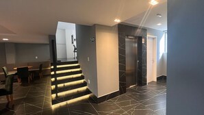 A modern hotel lobby with a staircase, a reception desk, and a sign indicating the elevator direction. - Flat Premium Legacy Suites - Cabo Branco (João Pessoa)