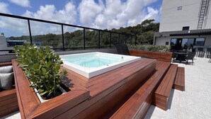 Una terrazza panoramica sul tetto con una vasca idromassaggio, sedute in legno e vista sul paesaggio circostante.