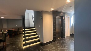 A modern hotel lobby with a staircase, a reception desk, and a sign indicating a no-smoking area. - Flat Gold Legacy Suites - Cabo Branco (João Pessoa)