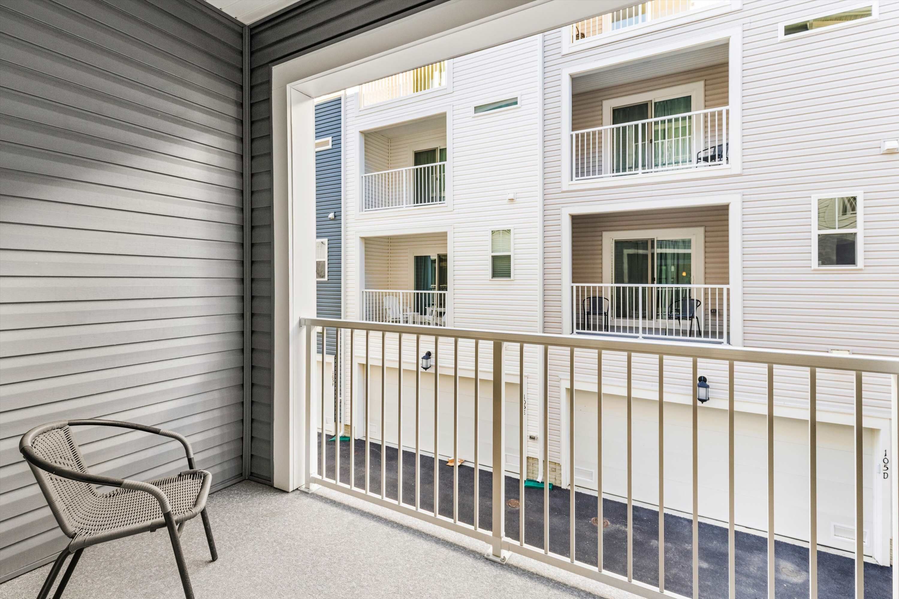 A balcony with a metal railing, a wicker chair, and a view of a multi-story building with balconies.