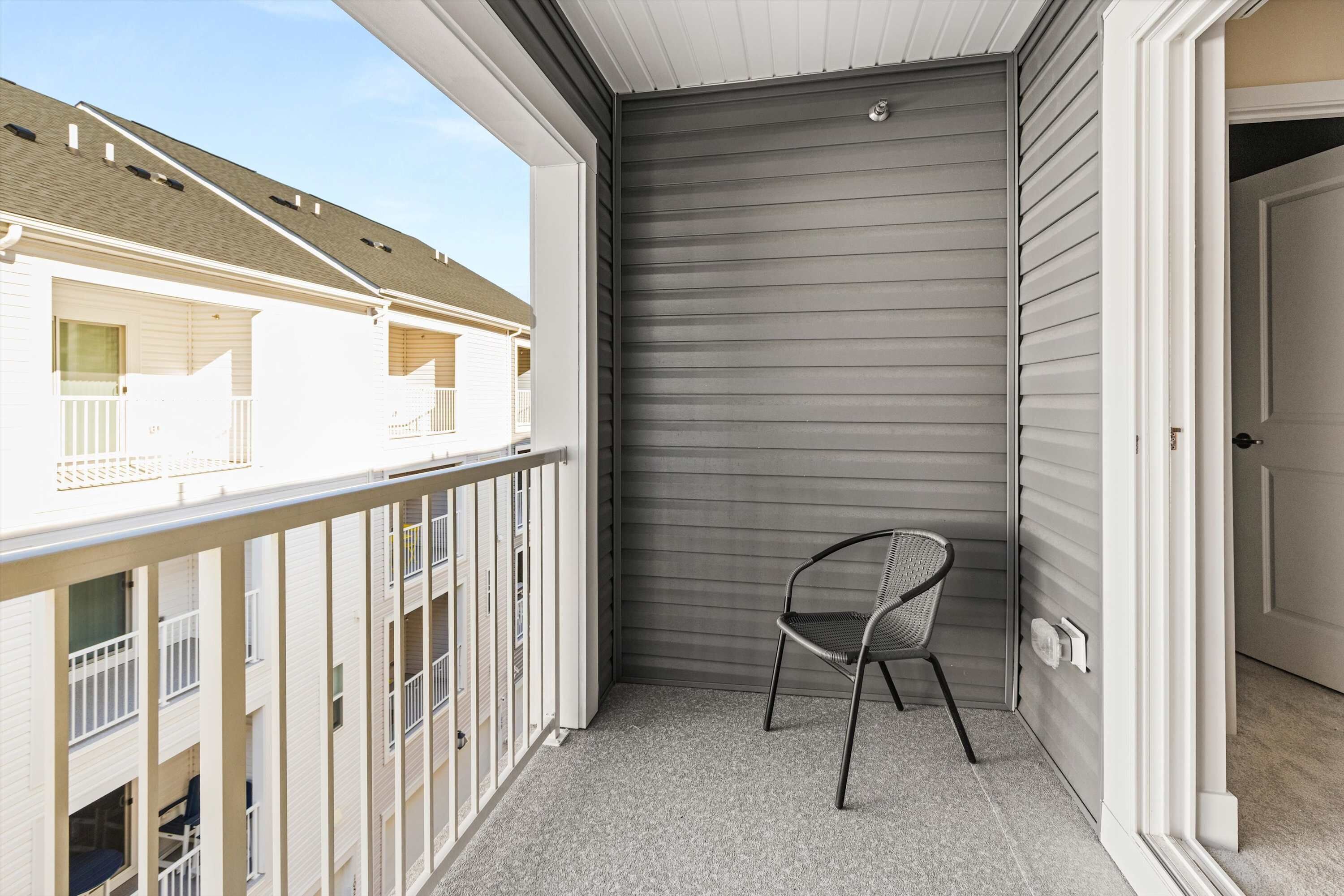 Ein Balkon mit einem Metallstuhl, einer geschlossenen Schiebetür und Blick auf benachbarte Gebäude.