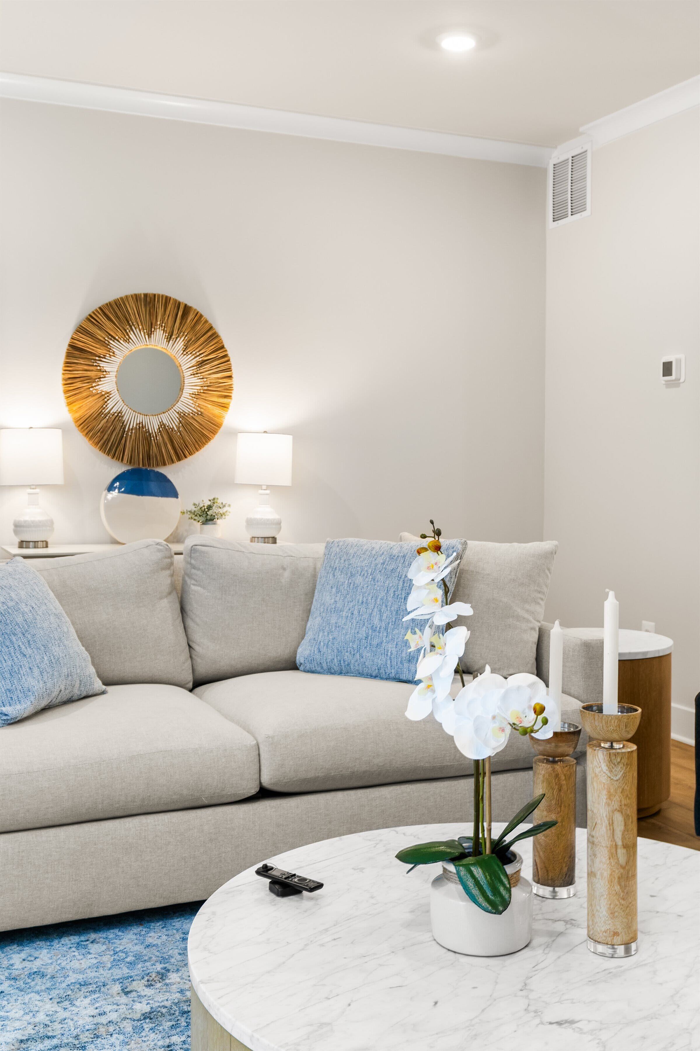 A modern living room with a beige sofa, a round coffee table, and a decorative mirror on the wall.