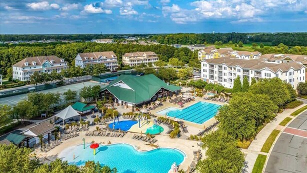 A resort with multiple buildings, a large swimming pool, and a tennis court. - Coastal Charm Estate | Pool, Golf + Luxury Style! (Selbyville)