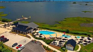 An aerial view of a waterfront hotel with a large swimming pool, outdoor seating, and a dock. - Coastal Charm Estate | Pool, Golf + Luxury Style! (Selbyville)