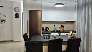 A modern kitchen with white cabinets, a stainless steel refrigerator, and a dining area with a table and chairs.