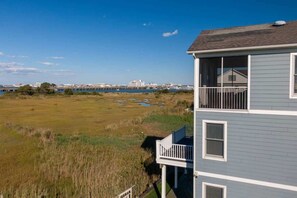 A two-story building with a balcony, overlooking a coastal area with a pier and buildings in the distance. - Anchor House | Pier, Boat Dock, & Gazebo Luxe Home (Ocean City)