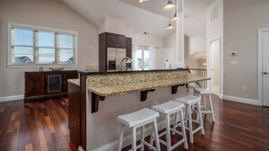 Une cuisine dotée d’un plan de travail en granit, de tabourets de bar blancs et de luminaires suspendus.