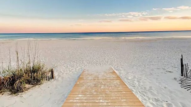 Une promenade en bois menant à une plage, avec un ciel dégagé.