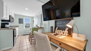 Une cuisine moderne avec des armoires blanches, un four à micro-ondes encastré et un coin repas agrémenté d’une chaise verte. On peut apercevoir un bureau avec une pancarte indiquant « Bienvenue à Beachview 306 » et une lampe.