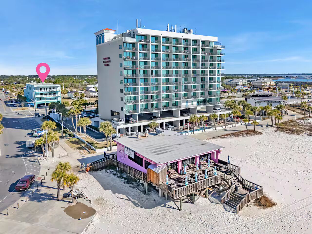 A beachfront hotel with a large building, a beachside bar, and a parking area.