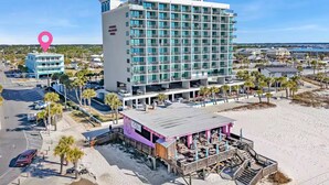 Un hôtel situé en bord de mer, doté d’un grand bâtiment, d’un bar au bord de la plage et d’un parking.