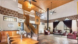 A spacious living area with a wooden dining table, red leather sofas, and a staircase leading to an upper level. - The Castle: Off-Grid Retreat nestled in the Sedgwick Valley 20 mins from Bendigo (Sedgwick)