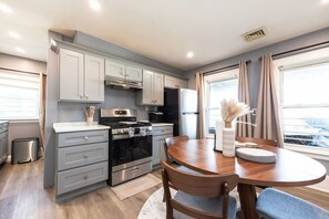 A modern kitchen with grey cabinets, a stainless steel stove, and a dining area with a round table and chairs. - Cozy 3BD/1BA in Boston | Franklin Zoo, Boston Comm (Boston)