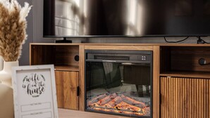 Een moderne woonkamer met een flatscreen televisie op een houten standaard, een inbouwplaats voor het vuur en een ingelijst bord op de tafel.