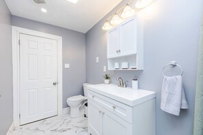 A bathroom with a white toilet, a white sink with a mirror above it, and a towel hanging on a metal ring. - Cozy 3BD/1BA in Boston | Franklin Zoo, Boston Comm (Boston)